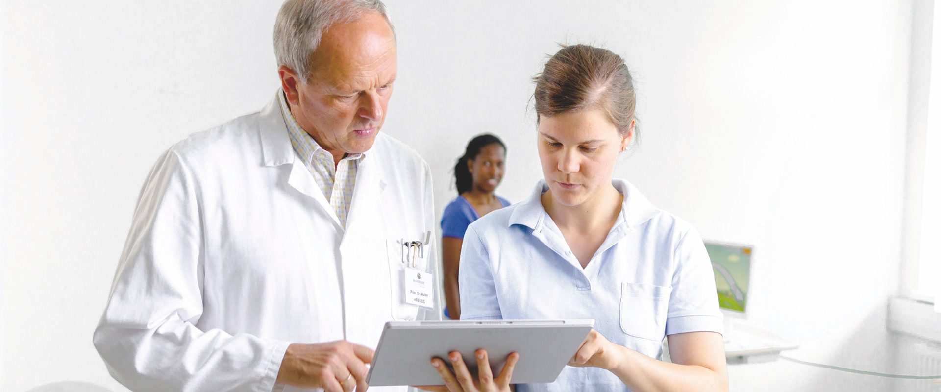 Arzt und Therapeutin schauen auf Diagnose, im Hintergrund sieht man eine Patientin