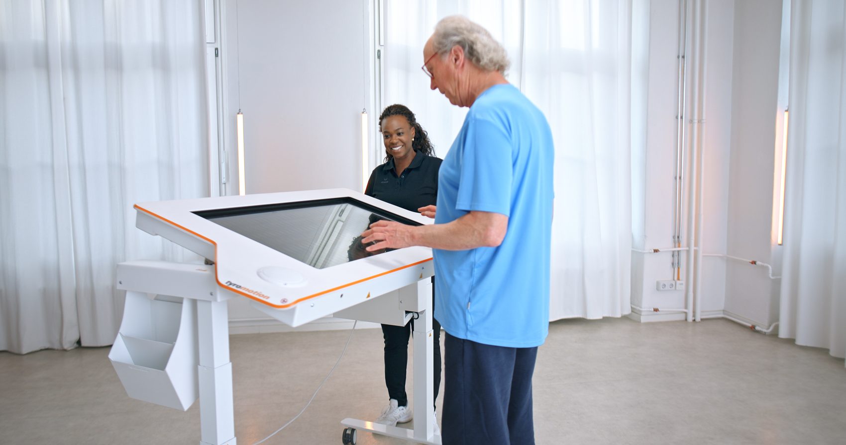 Older man stands beside a big touchscreen an lokks at it while a woman watches