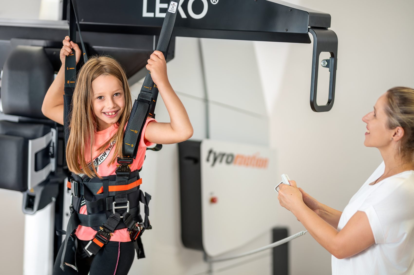 Young girl smiling in a gait training device with therapist standing aside