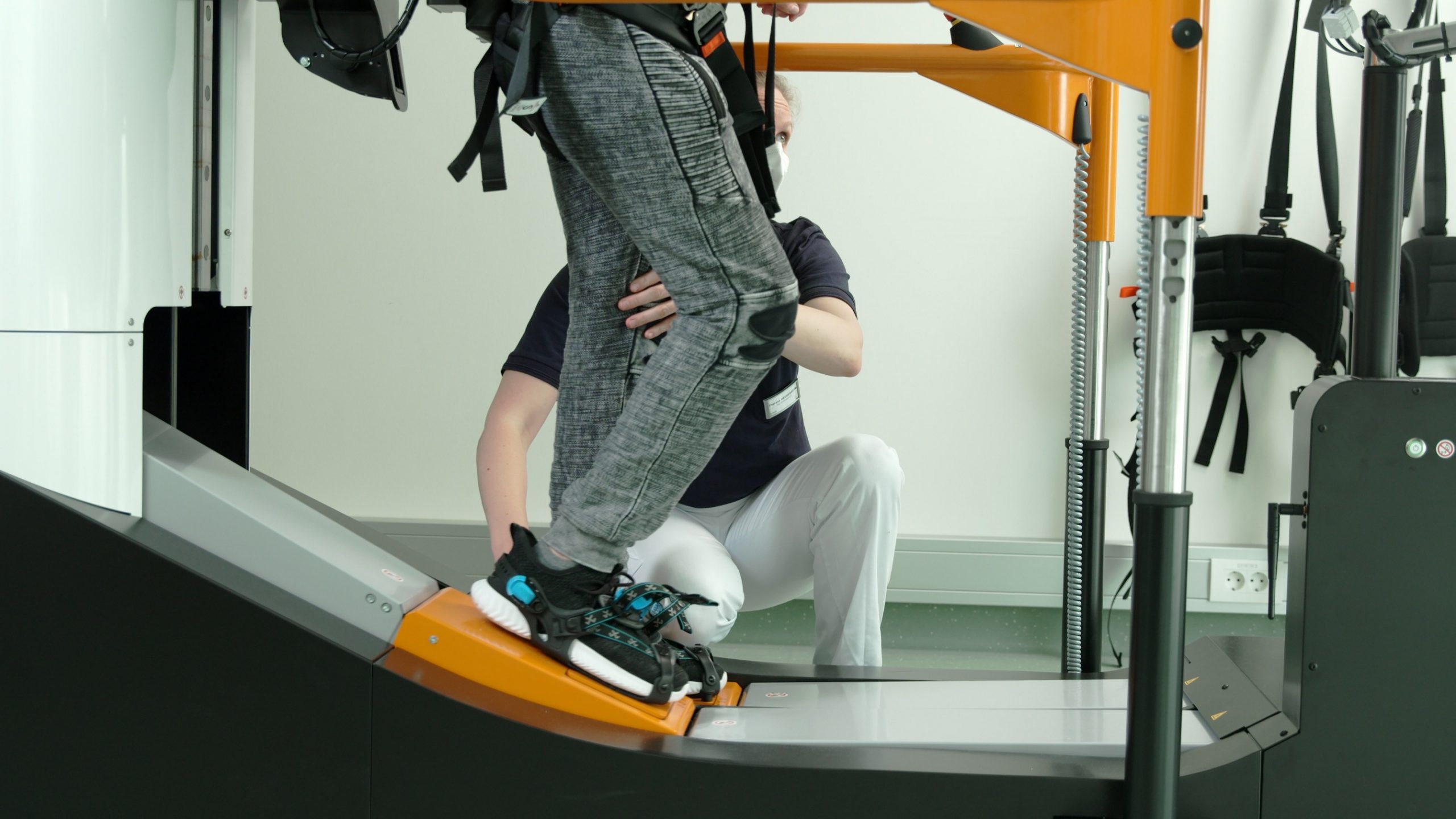Young man training on a gait trainer with help of therapist